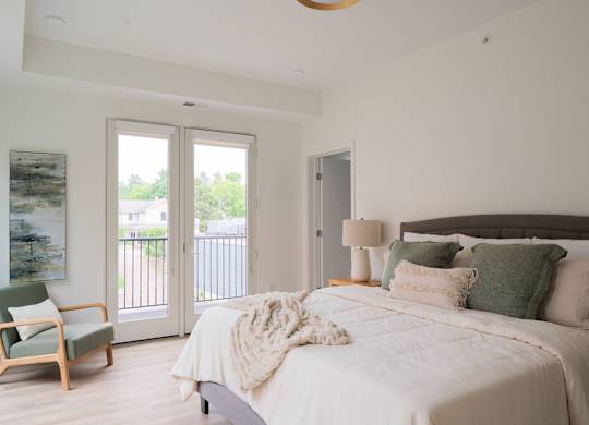 A bedroom with a bed, chair, and sliding glass doors.