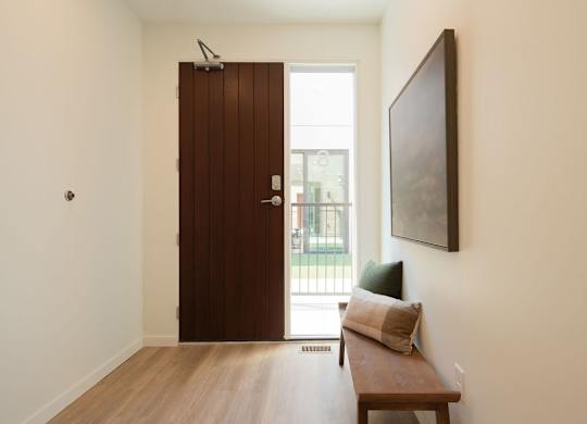 A brown door is in a room with a bench and a painting on the wall.