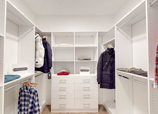 A white closet with clothes hanging and drawers underneath at One West Drive Apartments, Excelsior
