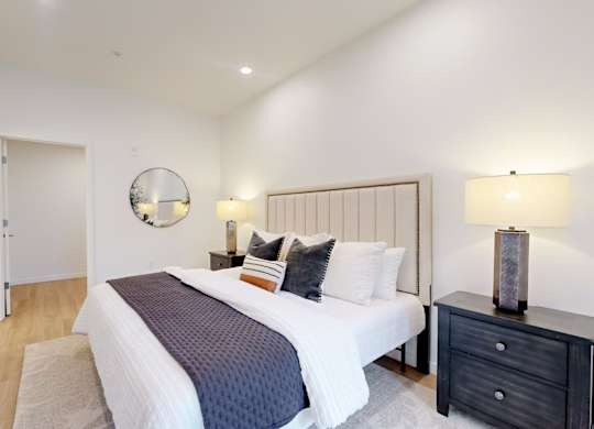 A bedroom with a large bed, a nightstand, and a mirror on the wall.