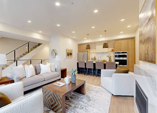 A modern living room with a staircase and a kitchen in the background.