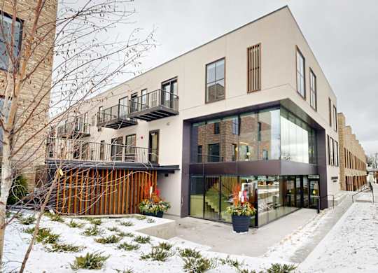 A modern building with a mix of beige and black exterior walls, large windows, and a balcony with a railing.