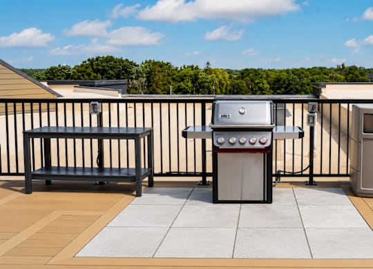 A BBQ grill is on a patio with a bench and a trash can.