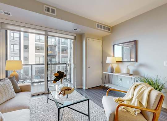 A living room with a white sofa, a glass coffee table, and a large window.