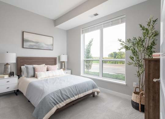 A bedroom with a large bed, two lamps, and a painting on the wall.at The Edison at Maple Grove, Maple Grove