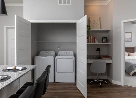 A laundry room with a washer and dryer is open to a bedroom.at The Edison at Maple Grove, Minnesota
