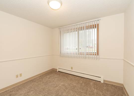 A room with a window covered by white blinds and a radiator on the floor.