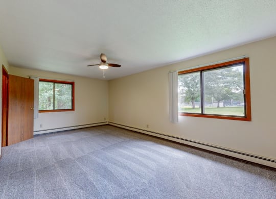 an empty living room with a ceiling fan and two windows