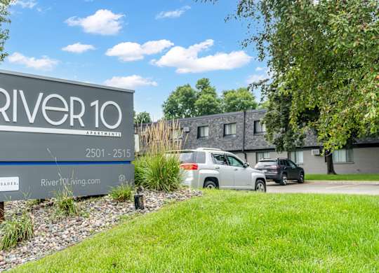 A sign for River10 is in front of a grassy area and some trees.