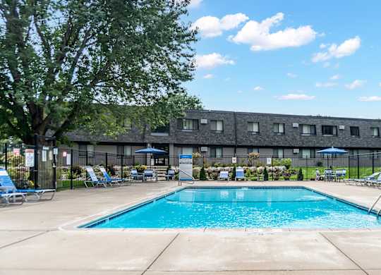 A swimming pool surrounded by lounge chairs and umbrellas in front of a building.
