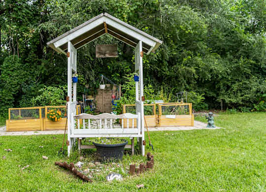 A small wooden structure with a porch and a yellow fence is surrounded by greenery.