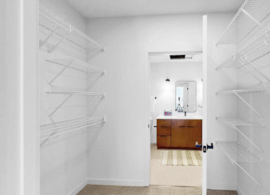A white walk-in closet with shelves and a wooden bench.