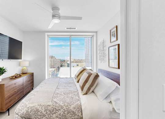 A bedroom with a bed, a dresser, and a window overlooking a cityscape.