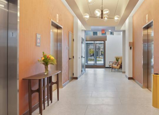 A hallway with a table and chairs on the left and a trash can on the right.