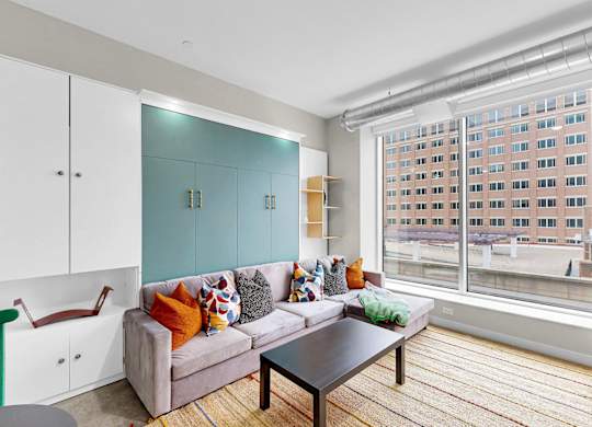 A living room with a couch, a coffee table, and a window with a view of a building.