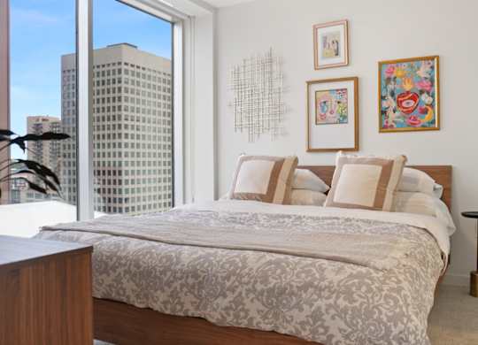 A bedroom with a large bed and a city view through the window.
