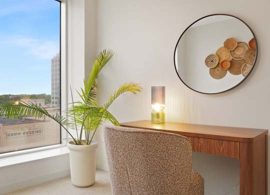 A room with a chair, a table, a plant, and a mirror with a decorative piece on it.
