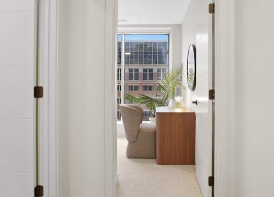 A white hallway with a door on the left and a chair and table in the distance.