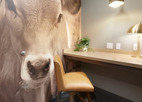 a cow painting on a wall next to a desk and a chair