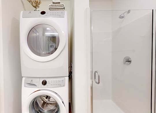 A white washing machine and dryer stacked on top of each other in a small laundry room.