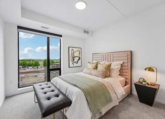 A bedroom with a large bed, a bench, and a window overlooking a parking lot.