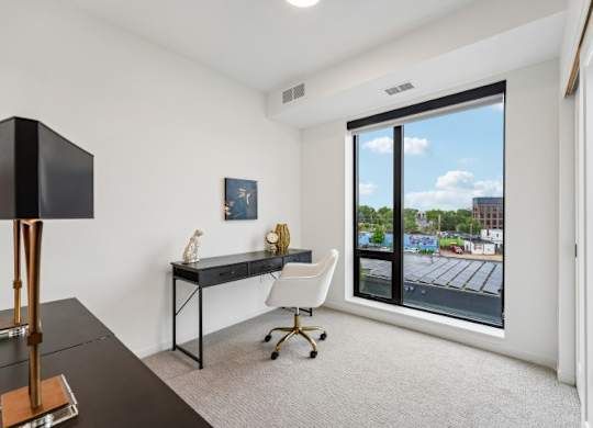 A room with a desk and chair with a window showing a parking lot.