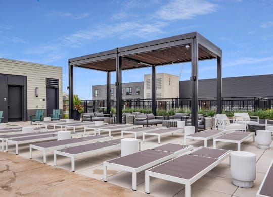 a group of white lounge chairs and umbrellas on a patio with buildings in the background