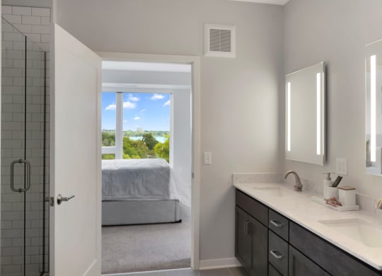 a bathroom with a large window and a bed in the background