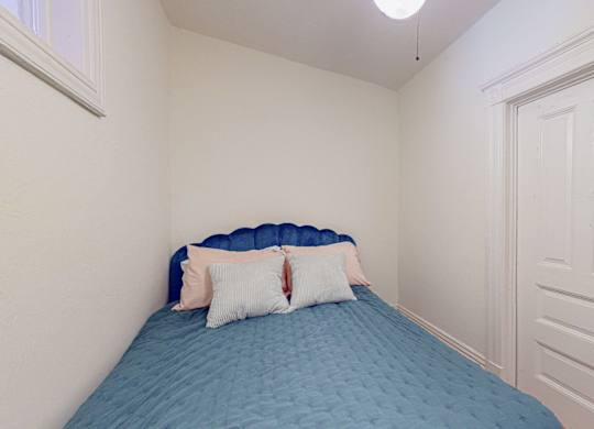 A bed with a blue cover and two pillows sits in a room with white walls.