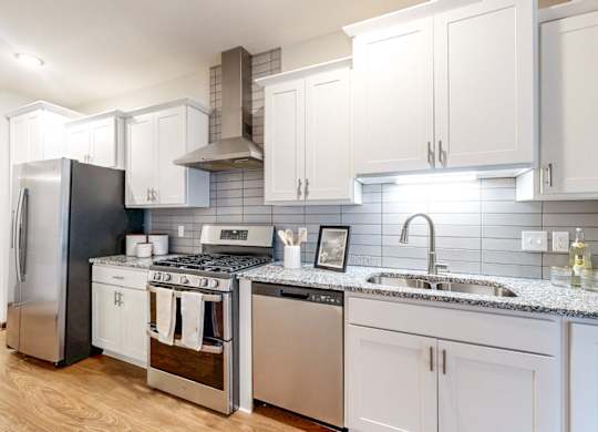 A modern kitchen with a stainless steel refrigerator, a stove with a cooking pot on it, and a sink with a faucet.