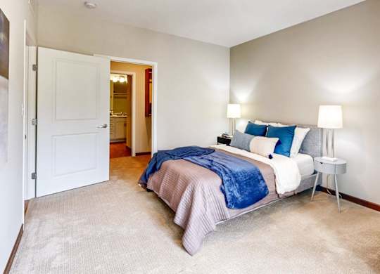 A bedroom with a bed, two lamps, and a carpeted floor.