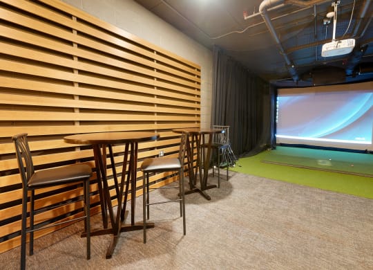golf simulator room with chairs, artificial turf and a projector screen