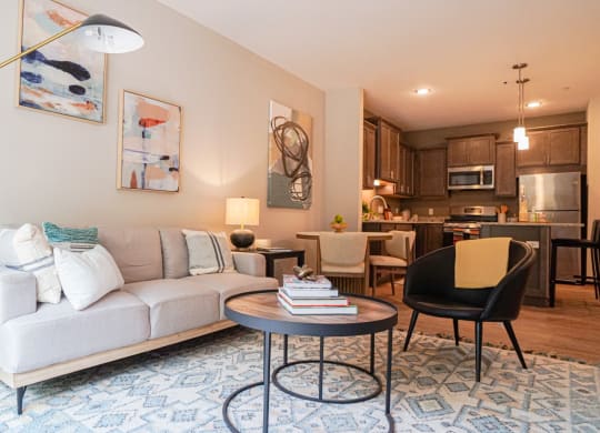 a living room with a couch table and chairs and a kitchen in the background at The Yards and Backyards, Saint Paul, MN