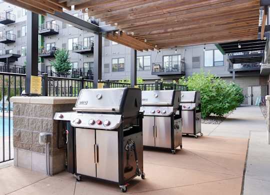 A patio with a grill and a pool in the background.