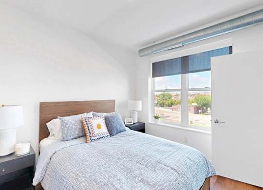 A bedroom with a bed, nightstand, and window.