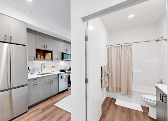 A modern kitchen with a refrigerator, cabinets, and a bathroom with a shower.