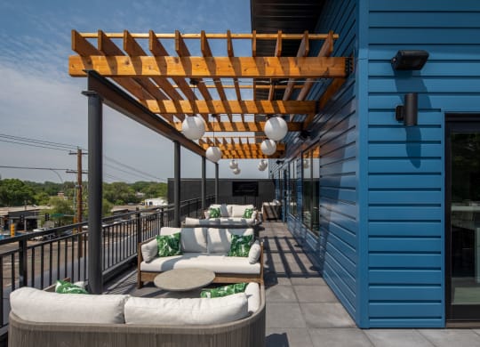 a wooden pergola on a balcony with white couches and green pillows
