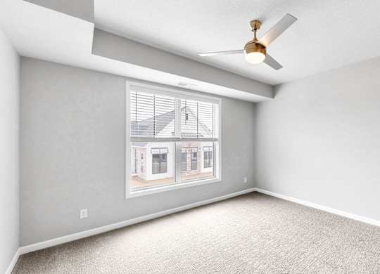 A room with a ceiling fan and a window showing a house.
