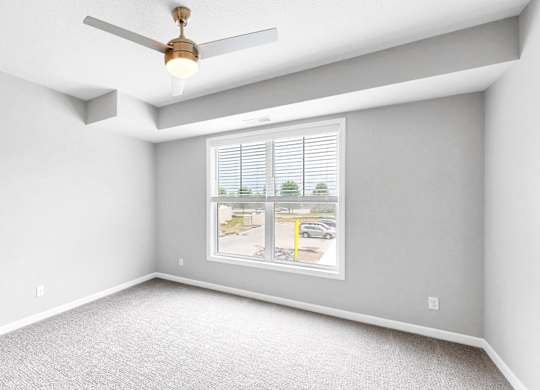 A room with a ceiling fan and a window showing a street view.