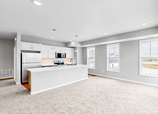 A spacious, empty room with a kitchen area and a window.