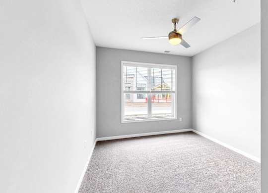 A room with a ceiling fan and a window overlooking a street.