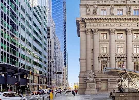 A large, ornate building stands in front of a modern glass building at One West,New York, 10004