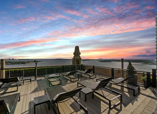 A rooftop patio with a table and chairs overlooking the water. at One West, New York