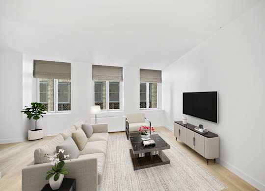 A living room with a grey couch, a coffee table, and a flat screen TV mounted on the wall at Aria, New York, 10038