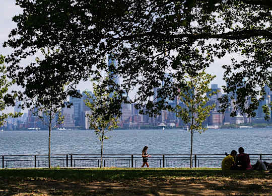 A couple is sitting on the grass by the water at Aria, New York, 10038