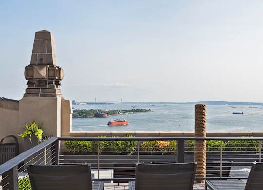 A balcony with chairs and a view of a bay with boats at One West,  New York,10004.