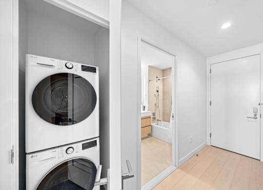 A white washing machine and dryer in a small laundry room at One West,  New York,10004.