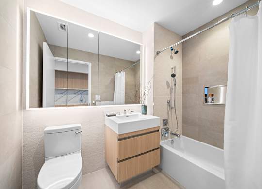 A modern bathroom with a white toilet, sink, and bathtub at One West,  New York,10004.