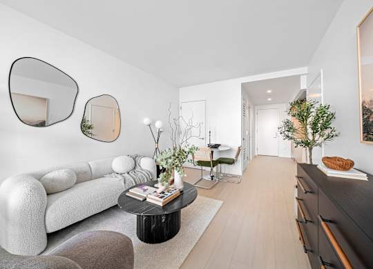 A modern living room with a white sofa, a black coffee table, and a large mirror on the wall at One West,New York, NY.