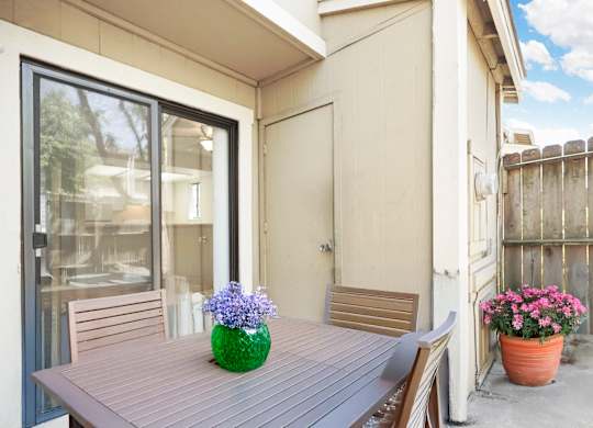 A table with a vase of flowers on it sits on a patio.
